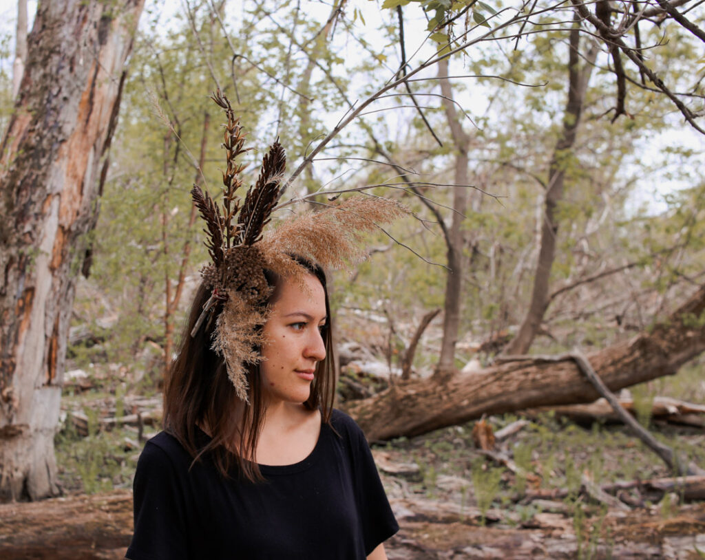woman with dried grasses and branches made into a large hair piece set in wooded forest.