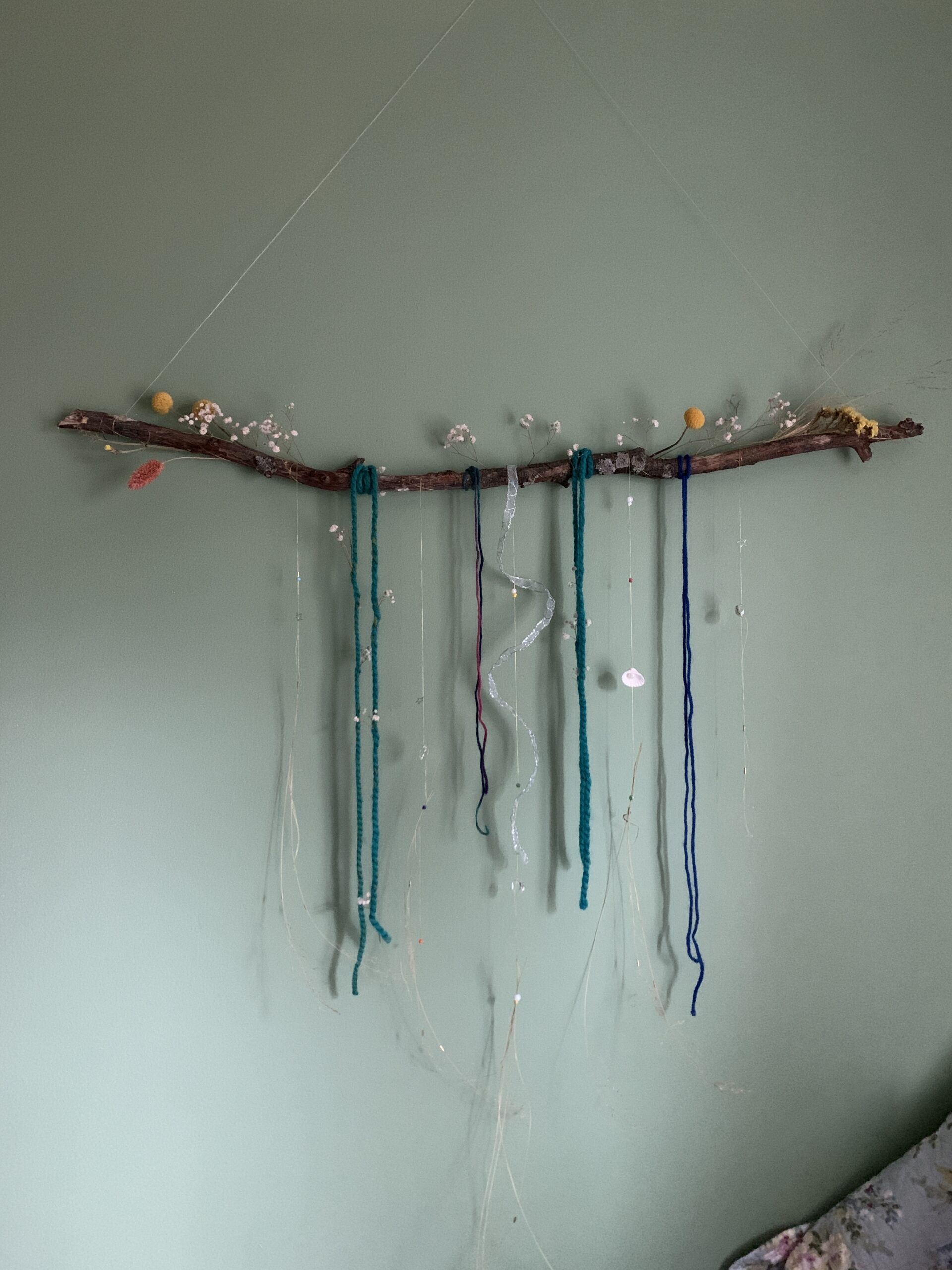 wooden branch with hanging yarn, string, and beads attached