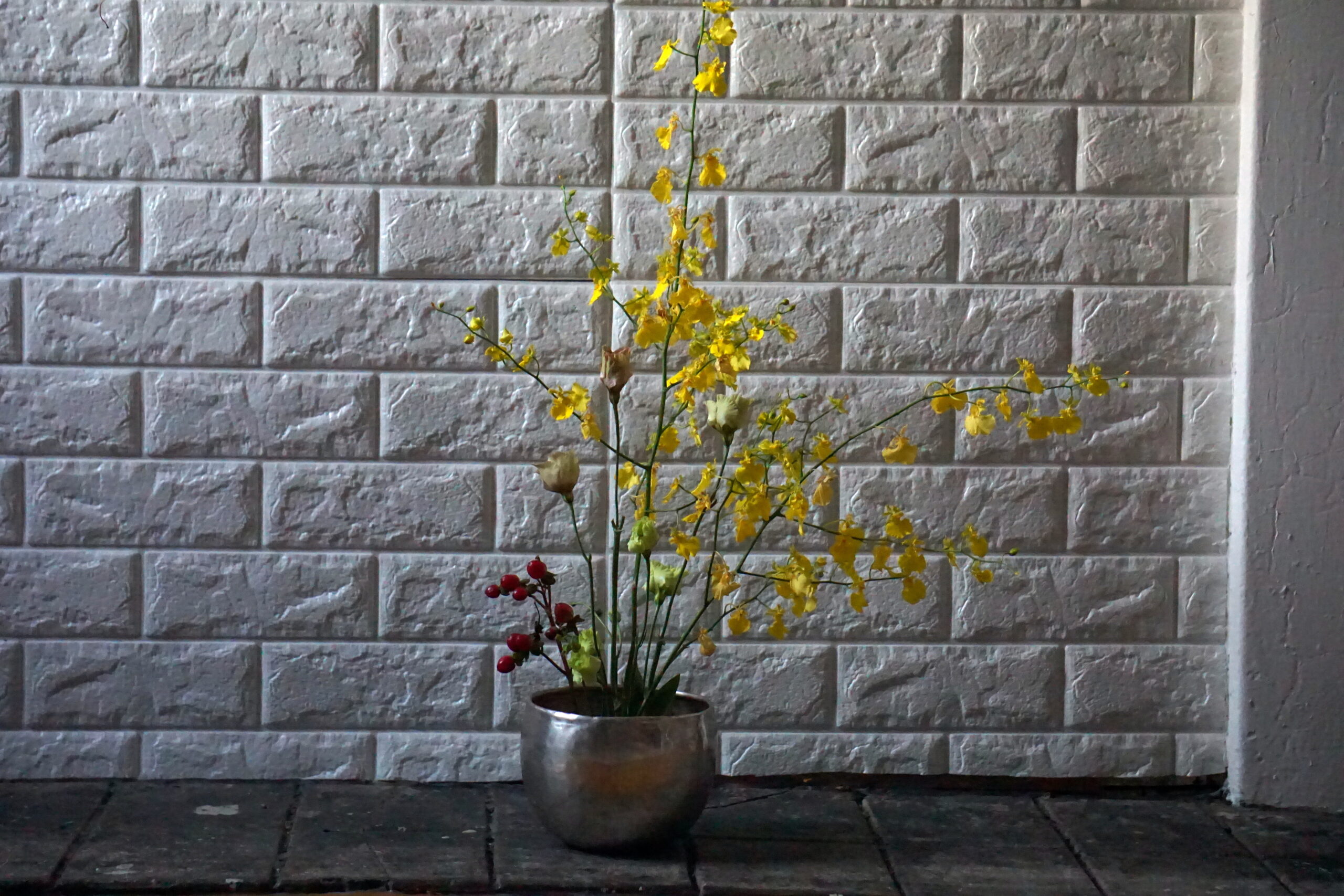 Yellow flowers with red berries arranged in silver bowl ikebana style with white background
